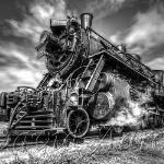 Old stream train pulling away from a grain elevator.